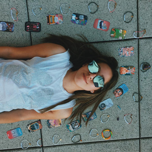 Model wearing Silver Lining Tank... its a white tank with silver wings. She is lying on the ground with tarot cards and bracelets around her.