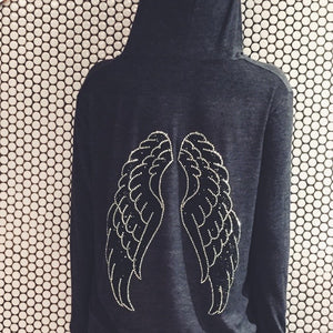 Grey hoodie with silver and black wings in front of a white and black circular tile wall. 