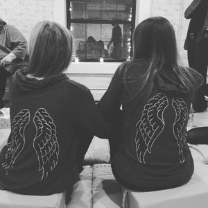 Mother daughter wearing matching grey hoodie with silver and black angel wings on the back. 