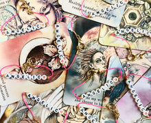 Load image into Gallery viewer, Photo of our Sweetheart Bracelet, on top of colorful, pretty tarot cards. The bracelet is a pink bracelet with white beads, and black font that says &quot;ANGELIC&quot;, and has a heart on the end. 