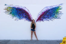 Load image into Gallery viewer, Black tank top with black wings, on the front, featured on a teenager girl standing in front of a mural with colorful angel wings. 