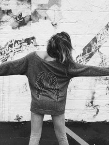 Black and white photograph of Cozy Comfy Crewneck. A grey speckled shirt with black and silver angel wings on the back. 