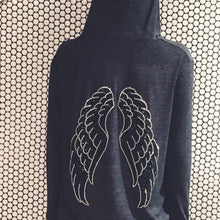Load image into Gallery viewer, Grey hoodie with silver and black wings in front of a white and black circular tile wall. 