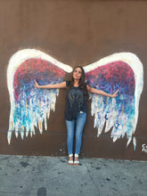 Load image into Gallery viewer, Girl wearing grey tank with silver and black wings against a colorful angel wing wall. 